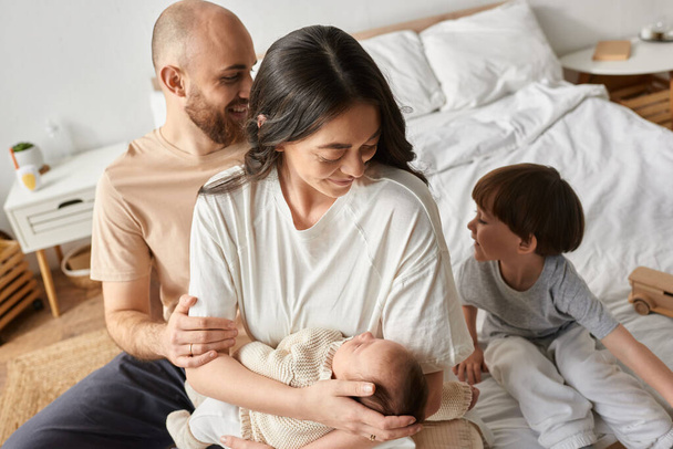 boldog anya tartja újszülött baba, míg a férje és fia mosolyogva egymásra - Fotó, kép