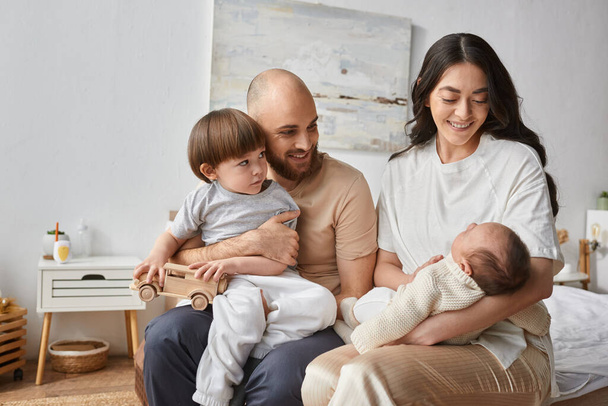 schöne moderne Familie in gemütlicher Homewear auf dem Bett sitzend und fröhlich lächelnd, Familienkonzept - Foto, Bild