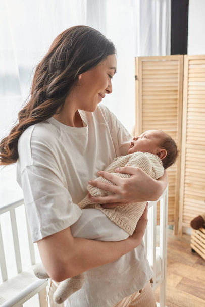 vertical shot of young beautiful mother holding her newborn baby and smiling at him lovingly, family - Photo, Image