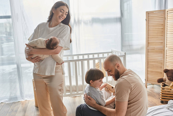 krásná matka drží svého chlapečka a láskyplně se dívá na svého manžela a syna, rodinný koncept - Fotografie, Obrázek