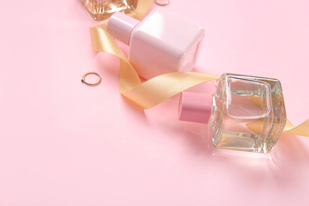ピンクの背景に香水ボトル,リング,ゴールデンリボン - 写真・画像