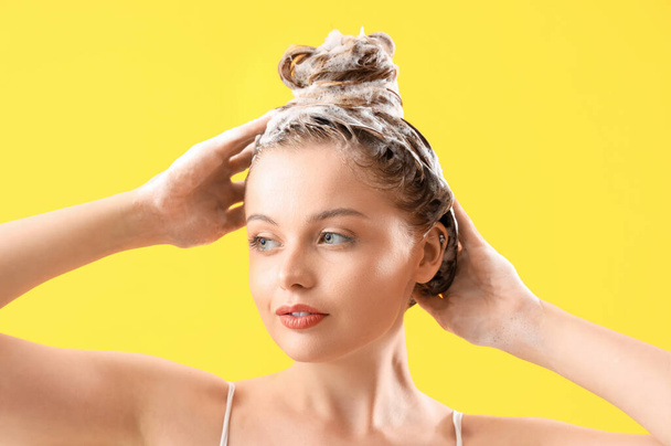 Mujer joven lavando el cabello sobre fondo amarillo, primer plano - Foto, Imagen