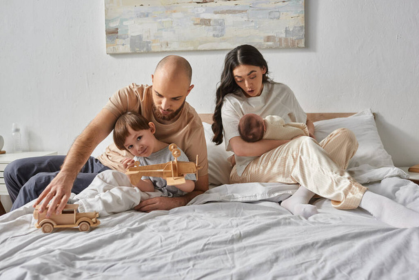 padre barbuto giocare con il suo piccolo figlio accanto a sua moglie in possesso di neonato, concetto di famiglia - Foto, immagini