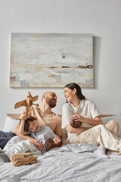 vertikální záběr moderních rodičů, jak na sebe šťastně hledí a tráví čas se svými dětmi - Fotografie, Obrázek