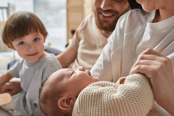 focus on cute newborn baby in arms of his mother next to blurred joyous little son, family concept - Photo, Image