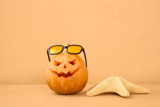 Carved pumpkin for Halloween with stylish sunglasses and starfish on orange background - Photo, Image