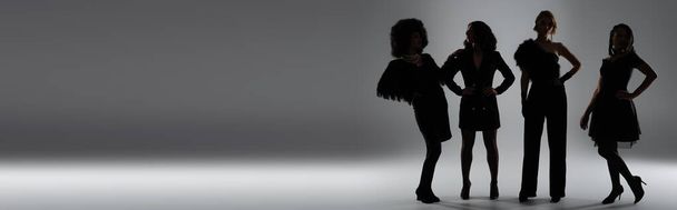 czarne sylwetki wielonarodowych dziewczyn w eleganckim stroju z dłońmi na biodrach na szarości, sztandar - Zdjęcie, obraz