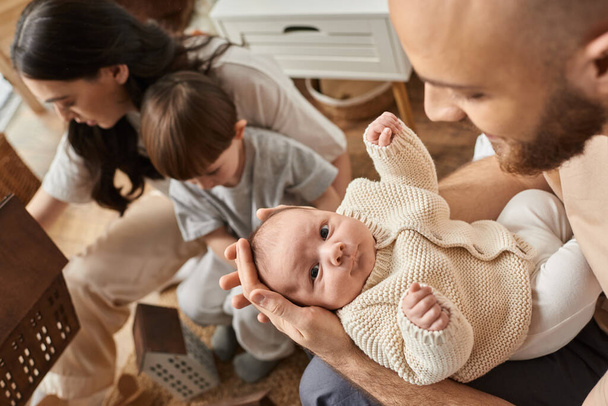 soustředit se na vousatý otec držet svého novorozeného chlapečka vedle jeho rozmazané manželky s jejich malým synem - Fotografie, Obrázek