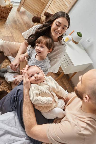 vertikale Aufnahme einer glücklichen Familie in gemütlicher Hauskleidung, die Zeit zusammen im Schlafzimmer verbringt, moderne Elternschaft - Foto, Bild