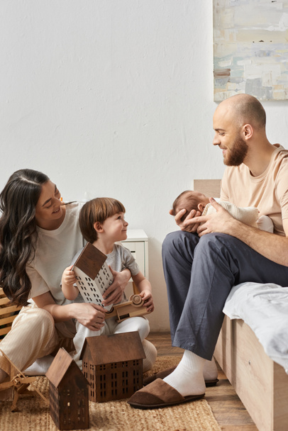 onnellisia nykyaikaisia vanhempia viihtyisissä kotivaatteissa viettää aikaa pienen poikansa ja vastasyntyneen vauvan, perheen kanssa. - Valokuva, kuva