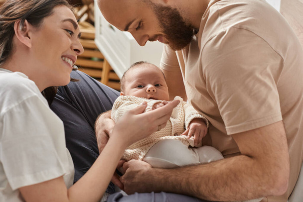 padres modernos alegres sosteniendo a su bebé recién nacido lindo y sonriéndole, concepto de familia - Foto, Imagen