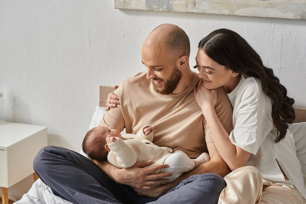 幸せな現代のカップルは抱擁し,愛情を持って彼らの愛らしい新生児の男の子,家族のコンセプトを見て - 写真・画像