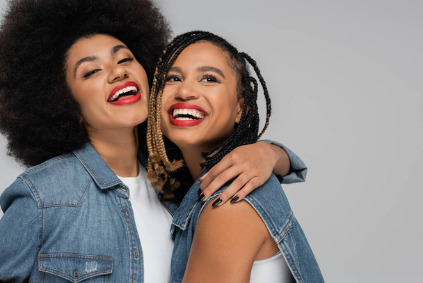 excited and stylish african american woman embracing girlfriend on grey backdrop, denim style - Photo, Image