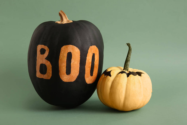 Calabazas de Halloween pintadas con palabra BOO y murciélagos sobre fondo verde - Foto, Imagen