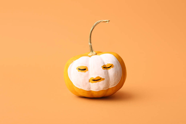 Pumpkin with drawn face and clay mask on orange background - Photo, Image