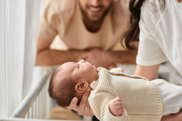 Bulanık sakallı, neşeli babasının yanında annesinin kollarında uzanan sevimli yeni doğan bebeğine odaklan. - Fotoğraf, Görsel