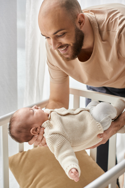 vertical shot of bearded happy father putting his newborn son into his crib, family concept - Photo, Image