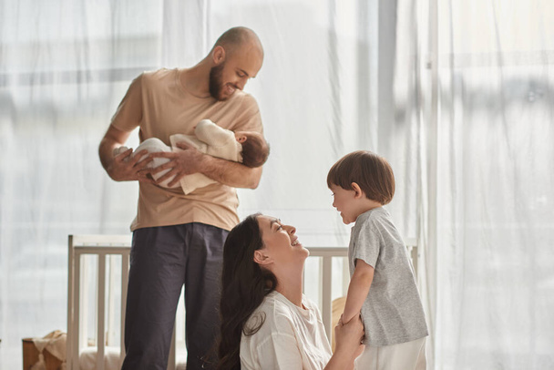 hilpeä kaunis neljän hengen perhe viihtyisissä kotivaatteissa viettää aikaa yhdessä onnellisesti, moderni vanhemmuus - Valokuva, kuva