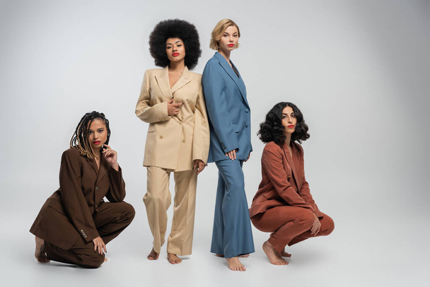 piena lunghezza di donne multietniche scalze in abiti colorati su grigio, moda e amicizia - Foto, immagini