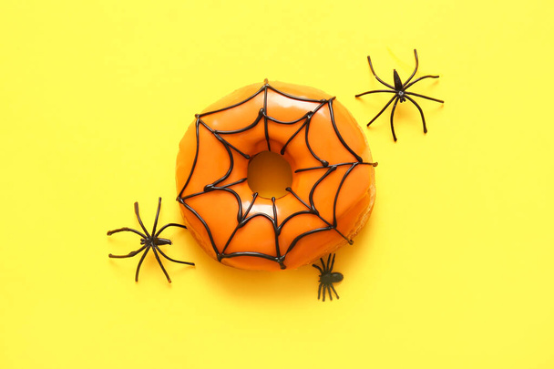 Tasty donut for Halloween with spiders on yellow background - Photo, Image