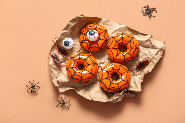 Tasty donuts for Halloween with eyes, spiders and candies on beige background - Photo, Image