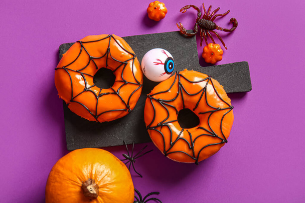 Tabuleiro de saborosos donuts com decorações para Halloween em fundo roxo - Foto, Imagem