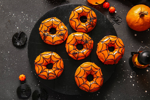 Lekkere donuts voor Halloween met spinnen, snoepjes, pompoen en lantaarn op zwarte achtergrond - Foto, afbeelding