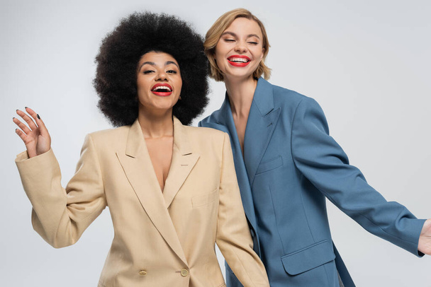 mulheres multirraciais alegres e na moda posando em ternos coloridos em pano de fundo cinza, beleza diversificada - Foto, Imagem