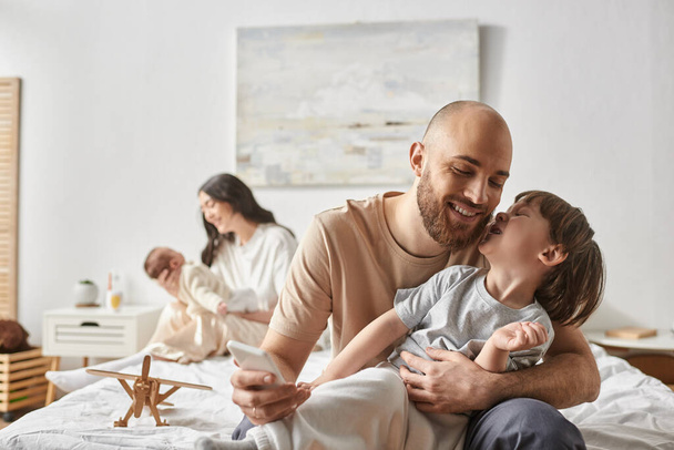 зосередьтеся на радісному батьку та його маленькому синові, розважаючись поруч зі своєю розмитою дружиною та дитиною на тлі - Фото, зображення
