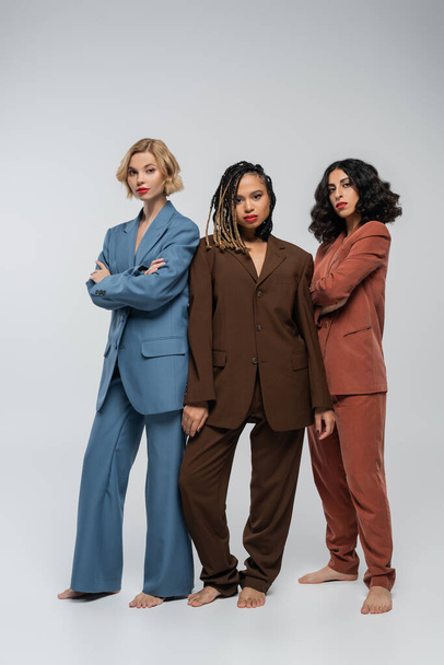 african american woman looking at camera near barefoot multiracial girlfriends in colorful suits - Photo, Image