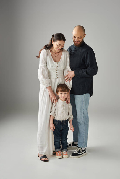 gut aussehende glückliche Eltern in edler Kleidung posieren mit ihrem kleinen Sohn vor grauem Hintergrund, Familie - Foto, Bild