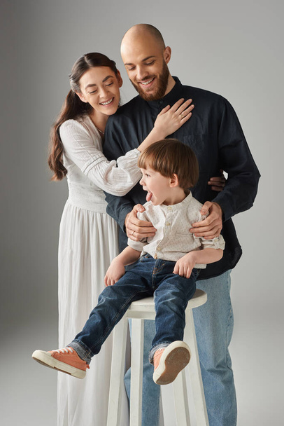 allegri genitori moderni che si abbracciano con la loro seduta su una sedia alta davanti a loro, concetto di famiglia - Foto, immagini