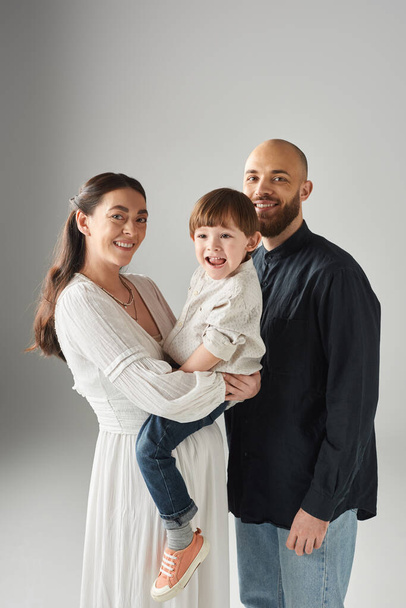 colpo verticale di famiglia allegra felice con bambino piccolo allegro in mani su sfondo grigio, famiglia - Foto, immagini
