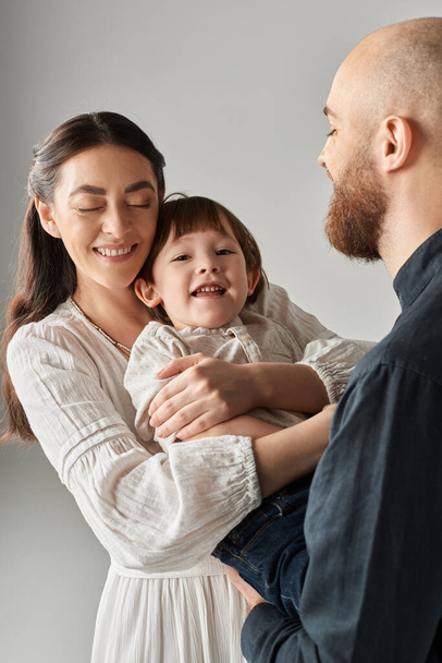 vertikale Aufnahme eines glücklichen Vaters, der auf seine fröhliche Frau blickt, die ihren kleinen entzückenden Sohn, die Familie, umarmt - Foto, Bild
