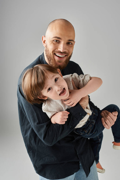 pionowe ujęcie radosnego ojca trzymającego wesołego syna i patrzącego szczęśliwie w kamerę, rodzinę - Zdjęcie, obraz