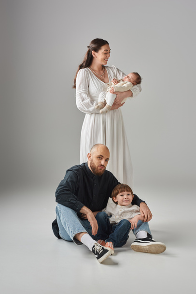 bearded father sitting on floor with his jolly little son next to his wife with their baby boy - Photo, Image
