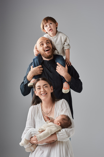 vrolijk moeder zitten met baby met haar man houden hun kleine zoon op schouders achter haar - Foto, afbeelding