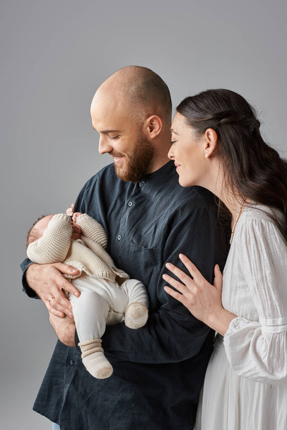 tiro vertical de padres felices en traje elegante mirando amorosamente a su bebé recién nacido, familia - Foto, Imagen