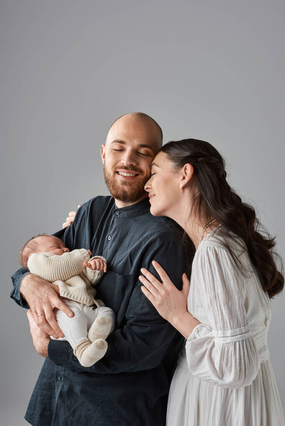 vertical shot of beautiful parents in classy outfits hugging and holding their newborn baby, family - Photo, Image