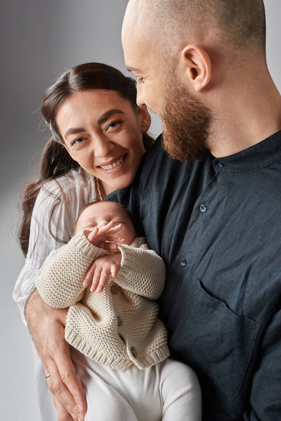 verticaal schot van bebaarde vader houden zijn baby jongen terwijl zijn gelukkige vrouw kijken naar camera, familie - Foto, afbeelding