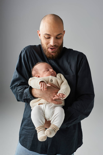 vidám apa elegáns öltözékben tartja az alvó újszülött baba szürke háttér, családi koncepció - Fotó, kép