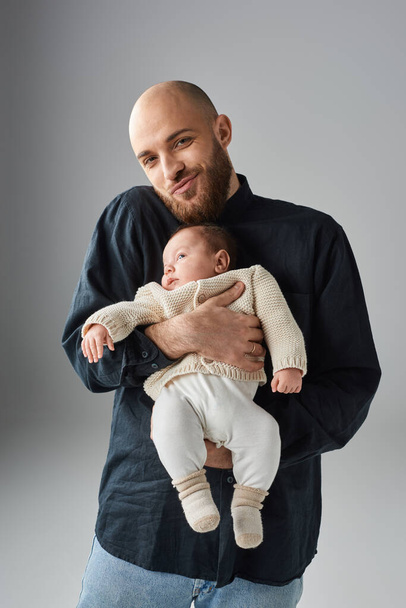 vertikální záběr vousatého pohledného muže držícího svého chlapečka a dívajícího se do kamery, rodinný koncept - Fotografie, Obrázek