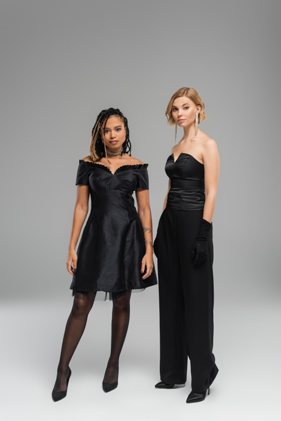 in voller Länge junge multirassische Frauen in schwarzer eleganter Kleidung vor grauem Hintergrund, vielfältige Schönheit - Foto, Bild