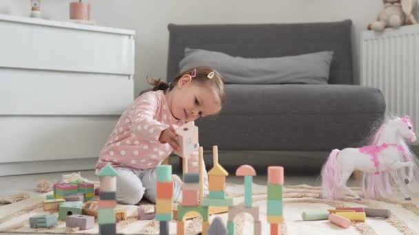 Egy kaukázusi lány kisgyermek játszik otthon a szobában fából készült játékokkal - Felvétel, videó