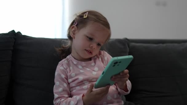 Ένα μικρό παιδί κορίτσι παίζει βιντεοπαιχνίδι στο κινητό τηλέφωνο smartphone - Πλάνα, βίντεο