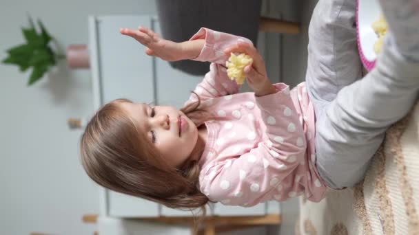 Ένα κορίτσι καυκάσιο παιδάκι τρώει μακαρόνια στο σπίτι με τα χέρια - Πλάνα, βίντεο