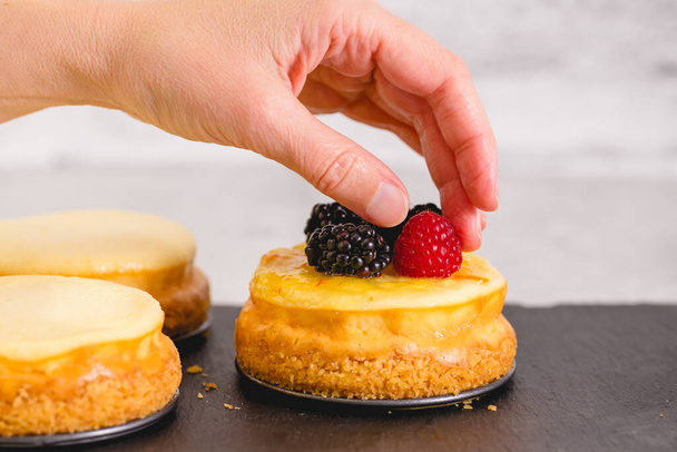 Vrouw topping cheesecake met verse frambozen en bramen. Zelfgemaakte mini kaastaart recept - Foto, afbeelding