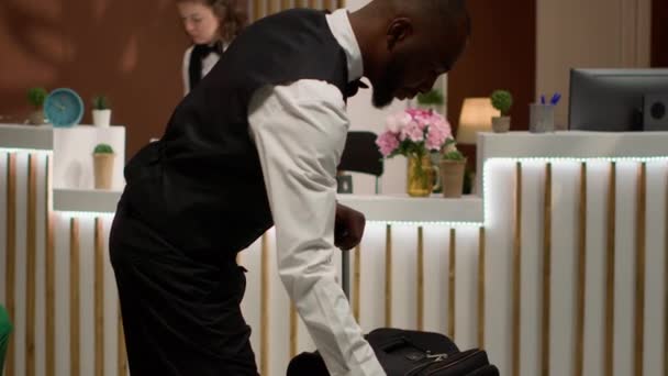 Afro-Amerikaanse piccolo draagt bagage om luxe service te bieden aan belangrijke zakenman hotelgasten. Beambte die in het resort arriveert om de conferentie bij te wonen, conciërge bijstand. - Video