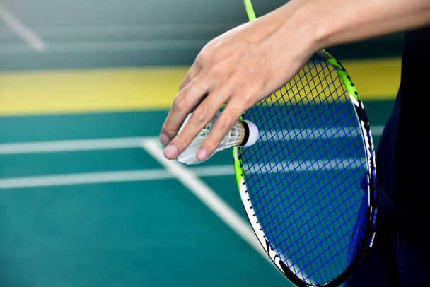 Le joueur de badminton tient une raquette blanche de badminton et une raquette de badminton devant le filet avant de le servir sur le filet vers un autre côté du terrain de badminton. Focus sélectif sur la navette blanche - Photo, image