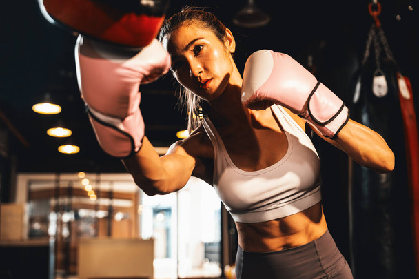 Die asiatische Muay Thai-Boxerin boxt in einem heftigen Boxtraining, schlägt ihren Sparringstrainer mit Schlaghandschuhen und demonstriert Muay Thai-Boxtechnik und -Geschick. Impulse - Foto, Bild